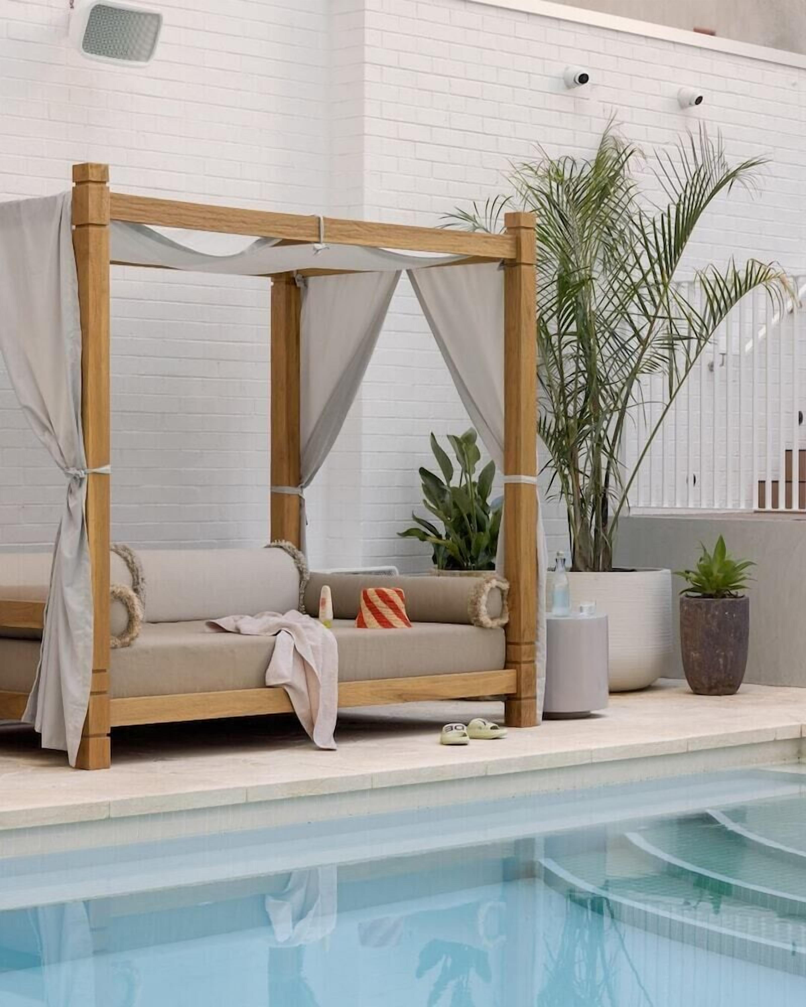A wooden daybed with a canopy, positioned by a poolside.