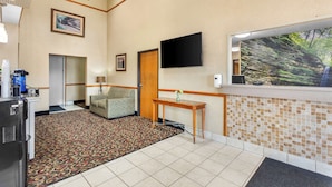 Um hall de hotel com carpete estampado, balcão de recepção, televisão na parede e janela com vista para árvores.