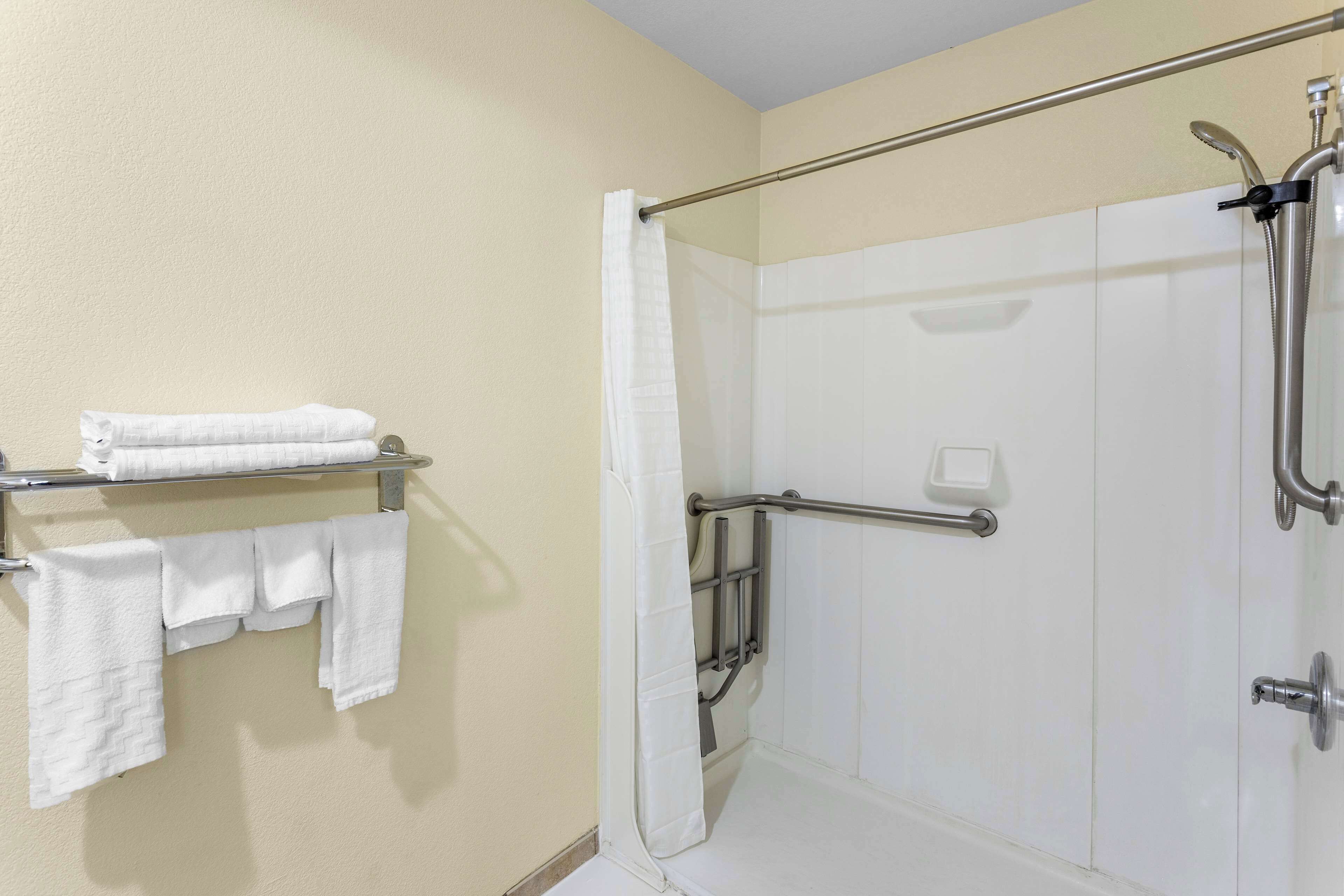 A bathroom with a shower, a towel rack with folded towels, and a handrail.