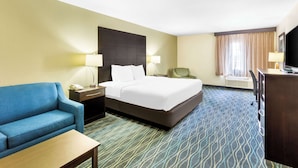Quarto de hotel com uma cama, um sofá azul, uma escrivaninha, uma cadeira e uma televisão.