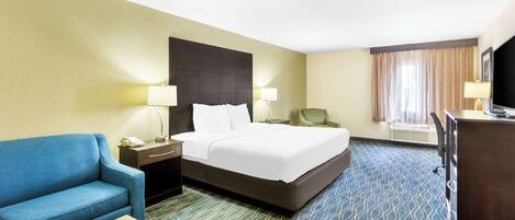 A hotel room with a bed, a blue sofa, a desk, a chair, and a TV.