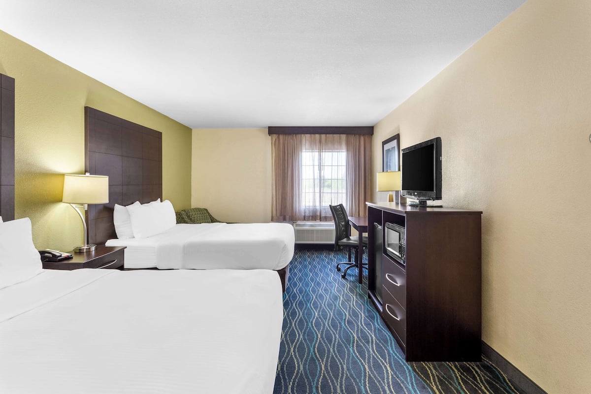 A hotel room with two beds, a desk with a TV, a lamp, and a window with curtains.