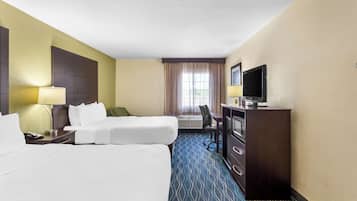 A hotel room with two beds, a desk with a TV, a lamp, and a window with curtains.