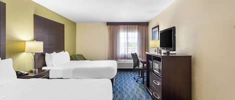 Habitación de hotel con dos camas, un escritorio con televisor, una lámpara y una ventana con cortinas.