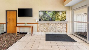 Um hall de hotel com balcão de recepção, televisão, janela ampla com vista para a natureza e piso de azulejos.