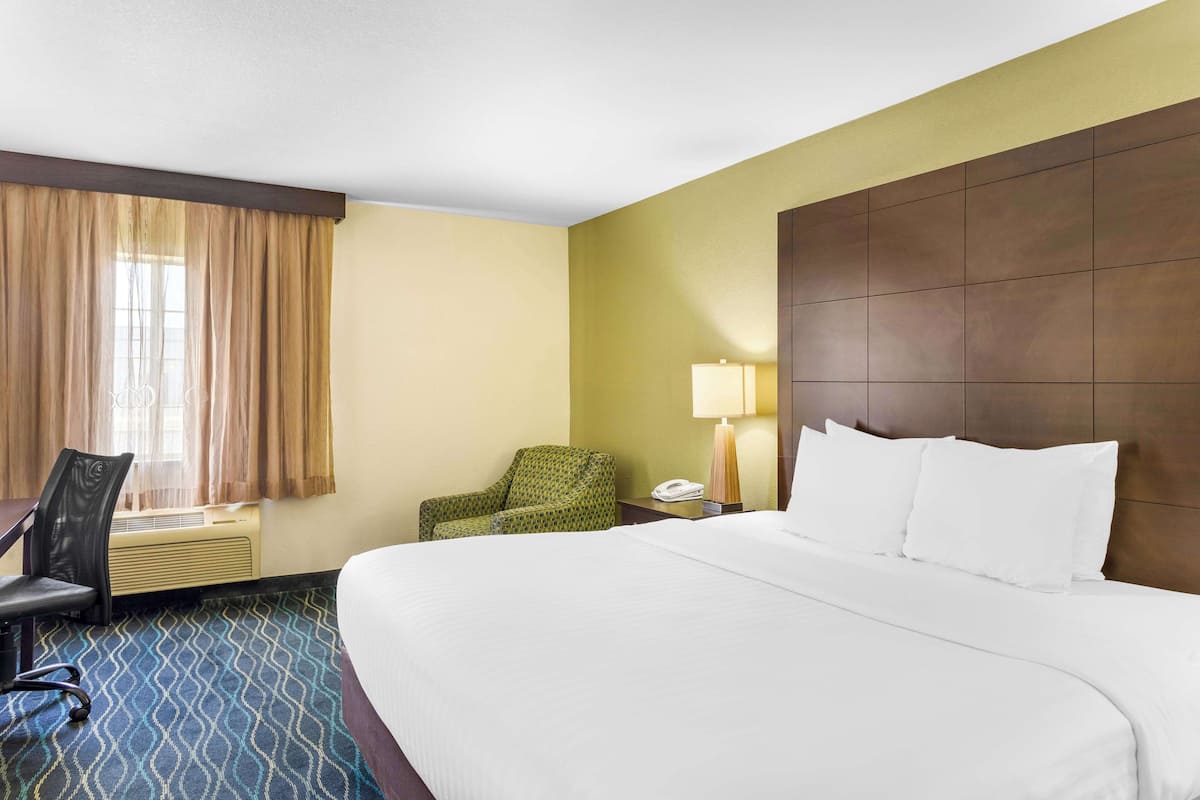 A hotel room with a large bed, a desk with a chair, a lamp, and a telephone.