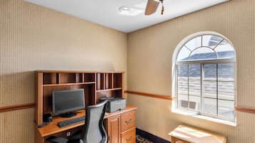 Een kamer met een houten bureau, computer, printer, een stoel, een klein tafeltje en een raam met uitzicht op de lucht.