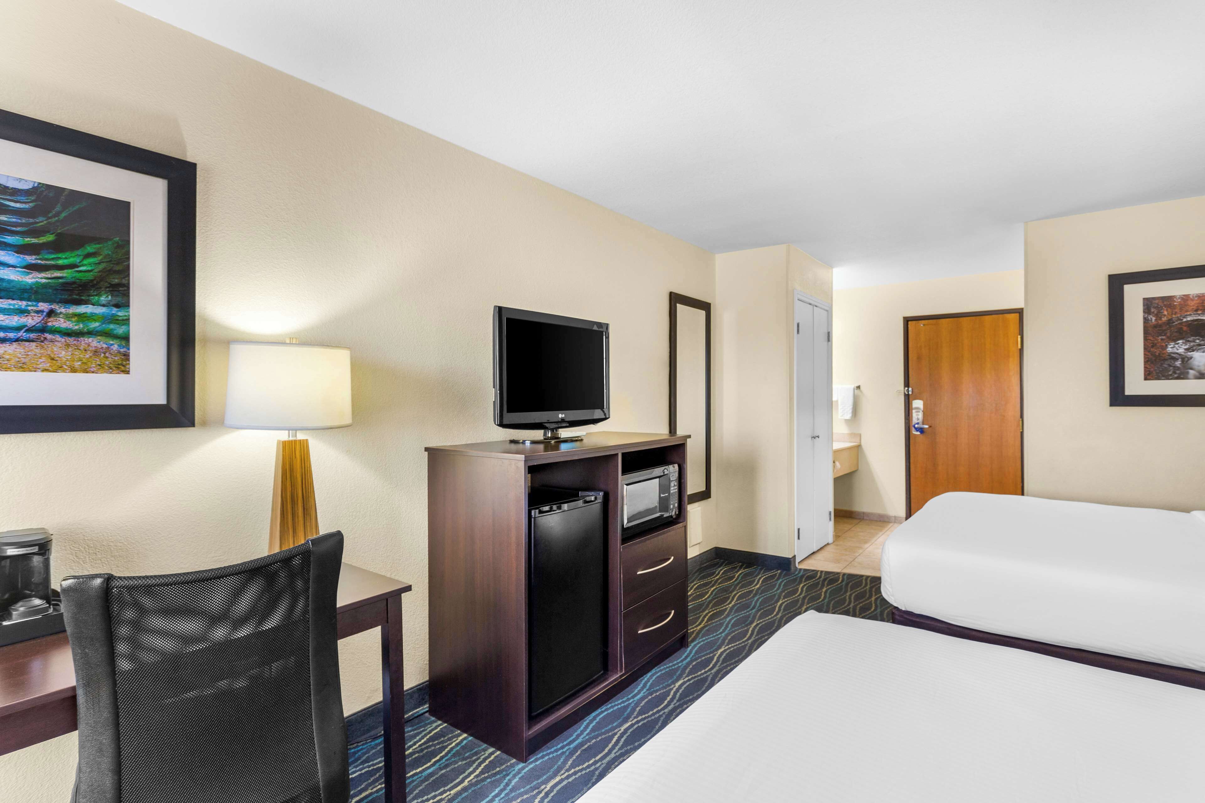 Une chambre d’hôtel comprenant un lit, un bureau avec une chaise, une télévision, un four à micro-ondes et une porte donnant accès à une salle de bain.