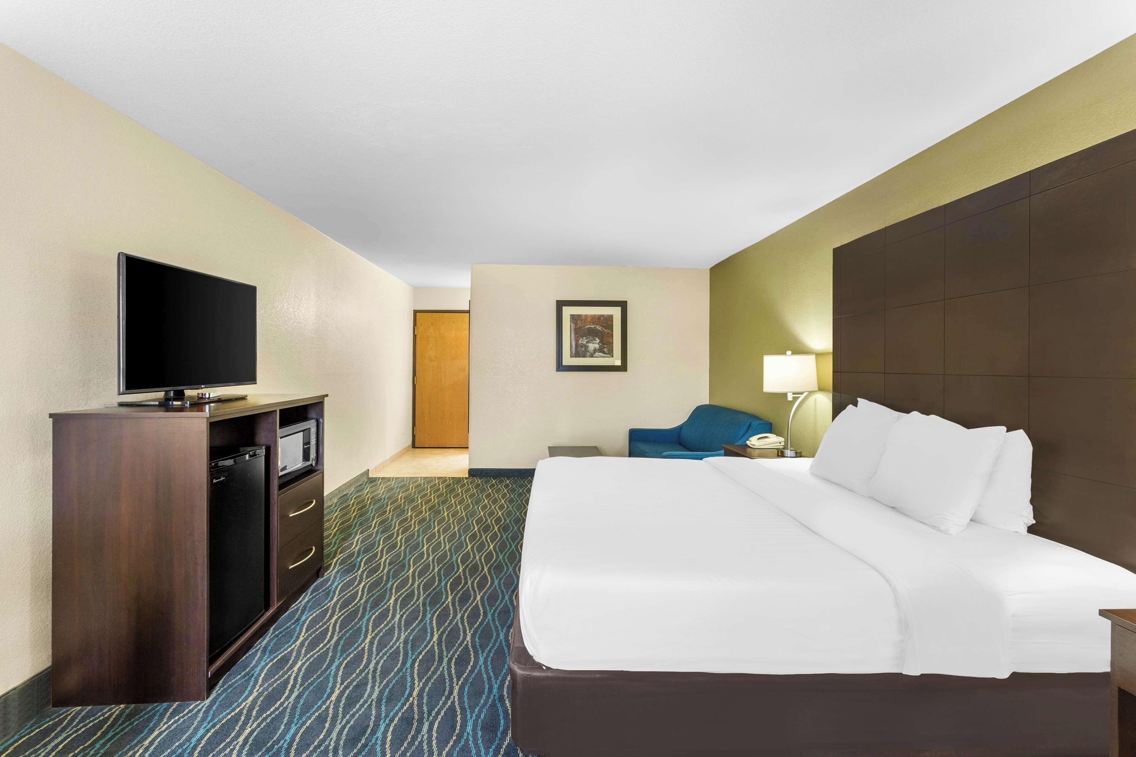 Habitación de hotel con cama, escritorio con televisor, una silla y una lámpara.
