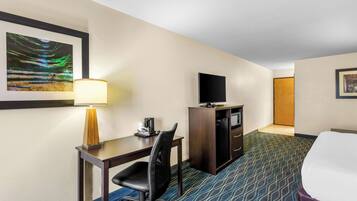 A hotel room with a desk, chair, TV, and bed.