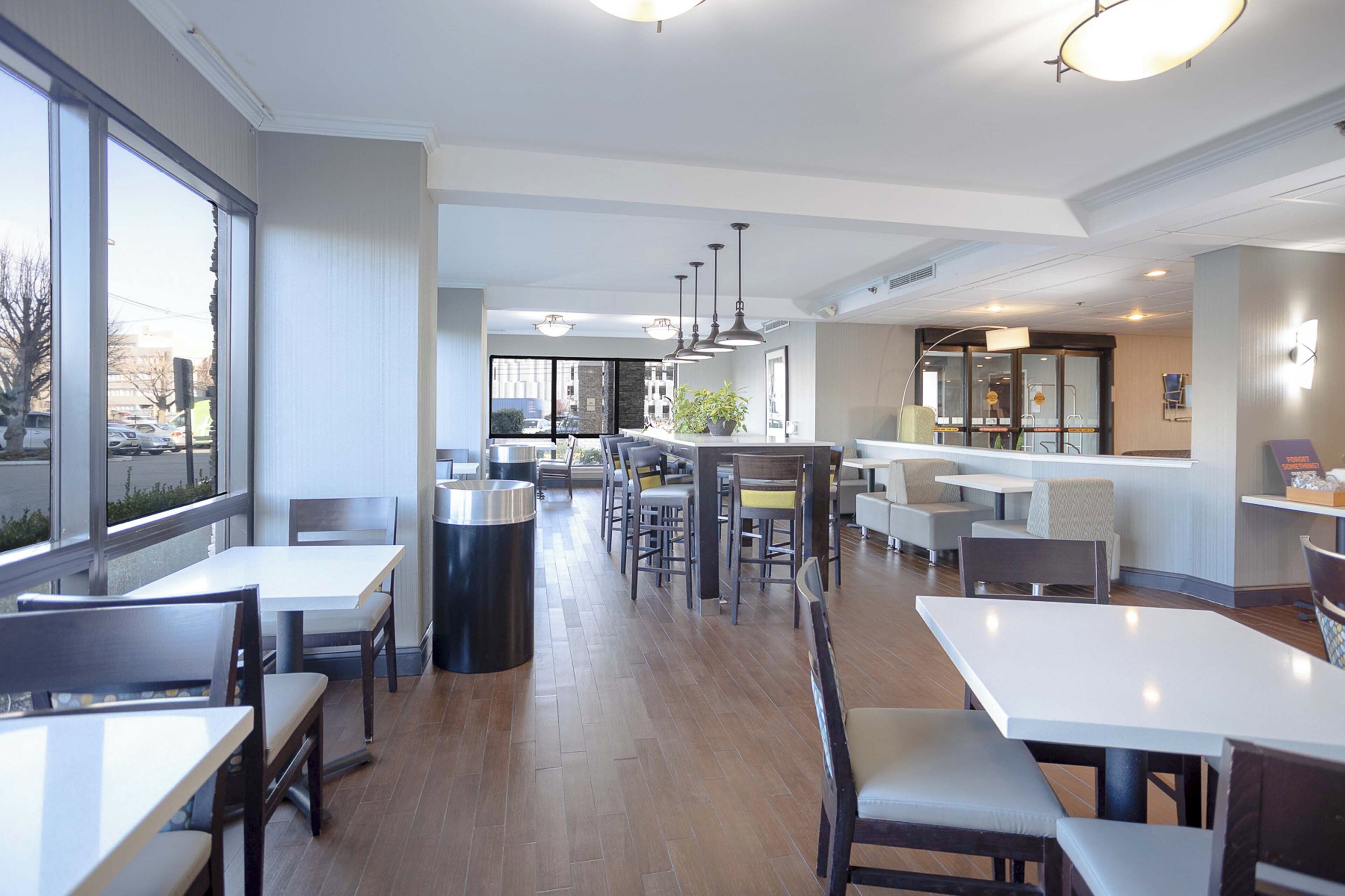Un restaurante moderno con techos altos, ventanas amplias y diversas opciones de asientos, incluyendo mesas y sillas.