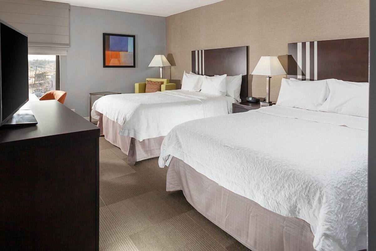 A hotel room with two beds, a desk, a chair, and a TV.