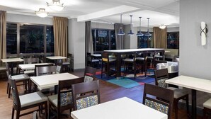 A modern dining area with multiple tables and chairs, large windows with curtains, and pendant lighting. - Holiday Inn Express Newark Airport Elizabeth by IHG (Elizabeth)
