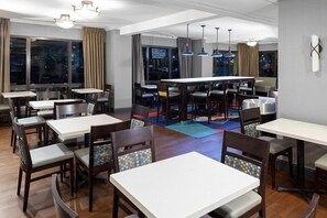 A modern dining area with multiple tables and chairs, large windows with curtains, and pendant lighting. - Holiday Inn Express Newark Airport Elizabeth by IHG (Elizabeth)