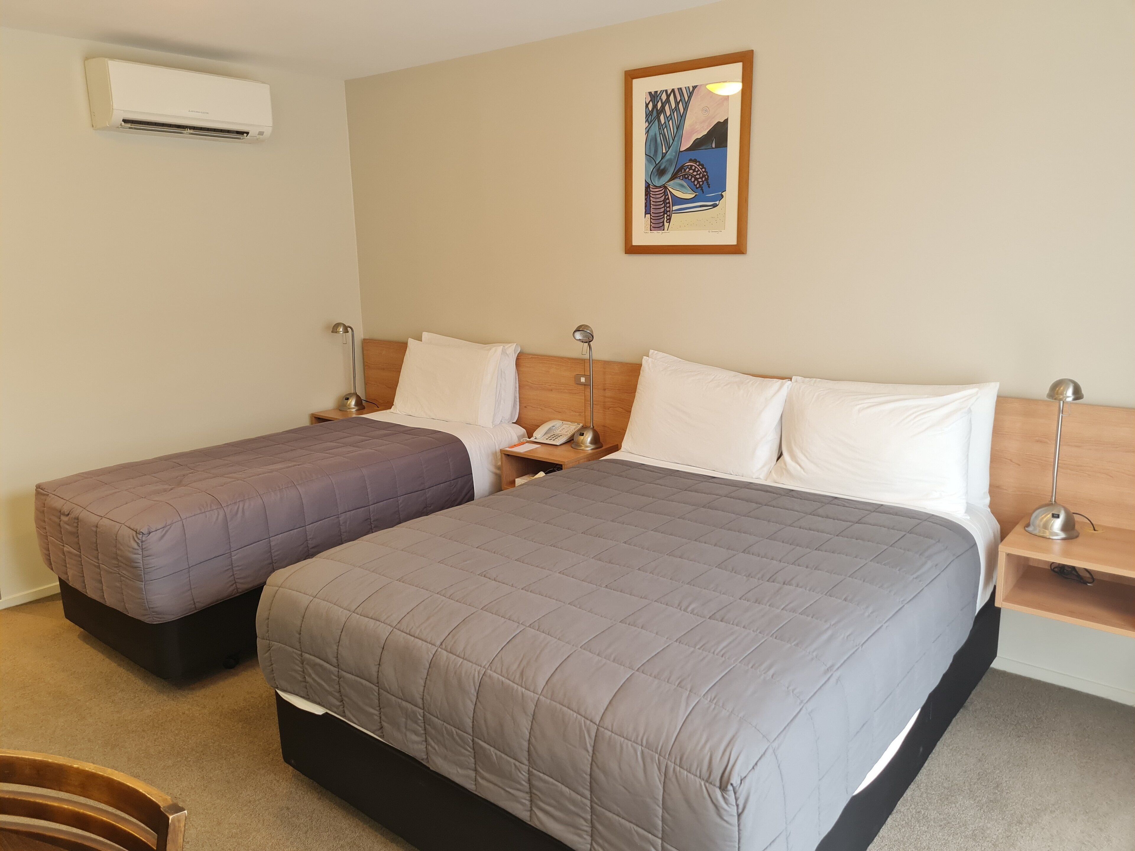 A hotel room with two beds, a painting on the wall, and an air conditioner.
