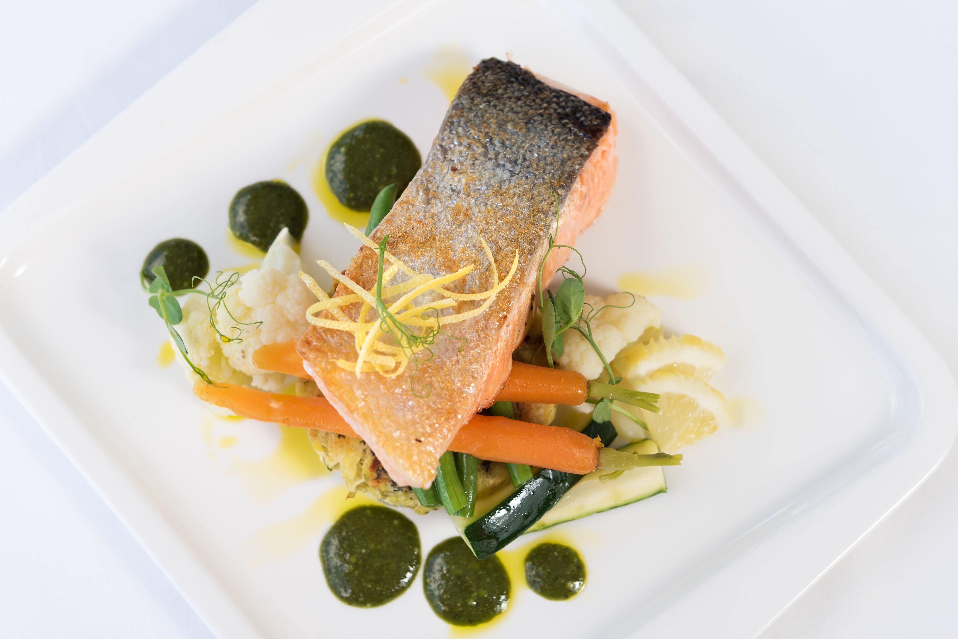 Un plato blanco con salmón, verduras y salsa verde.