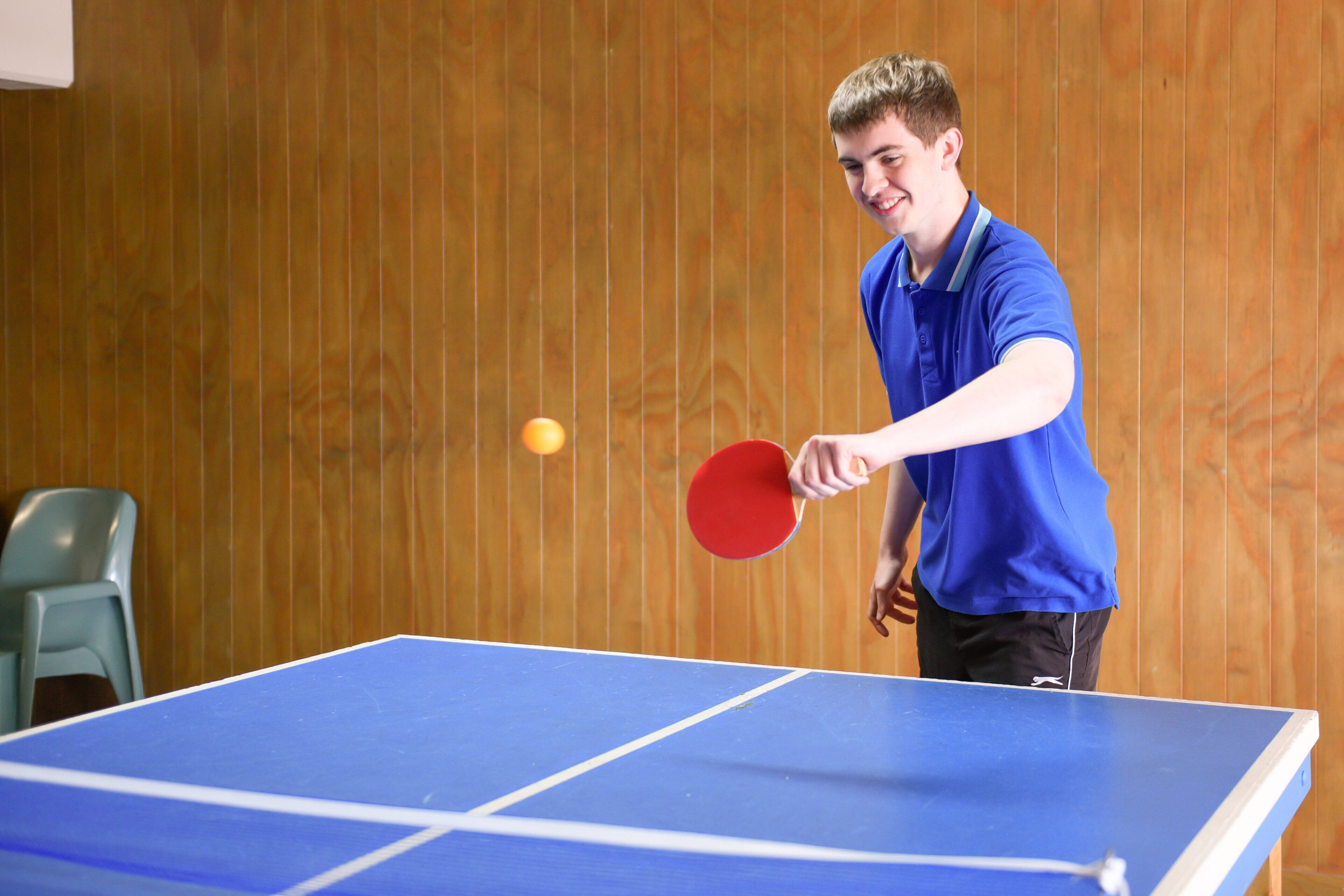 A person playing table tennis in a room with wooden panel walls.