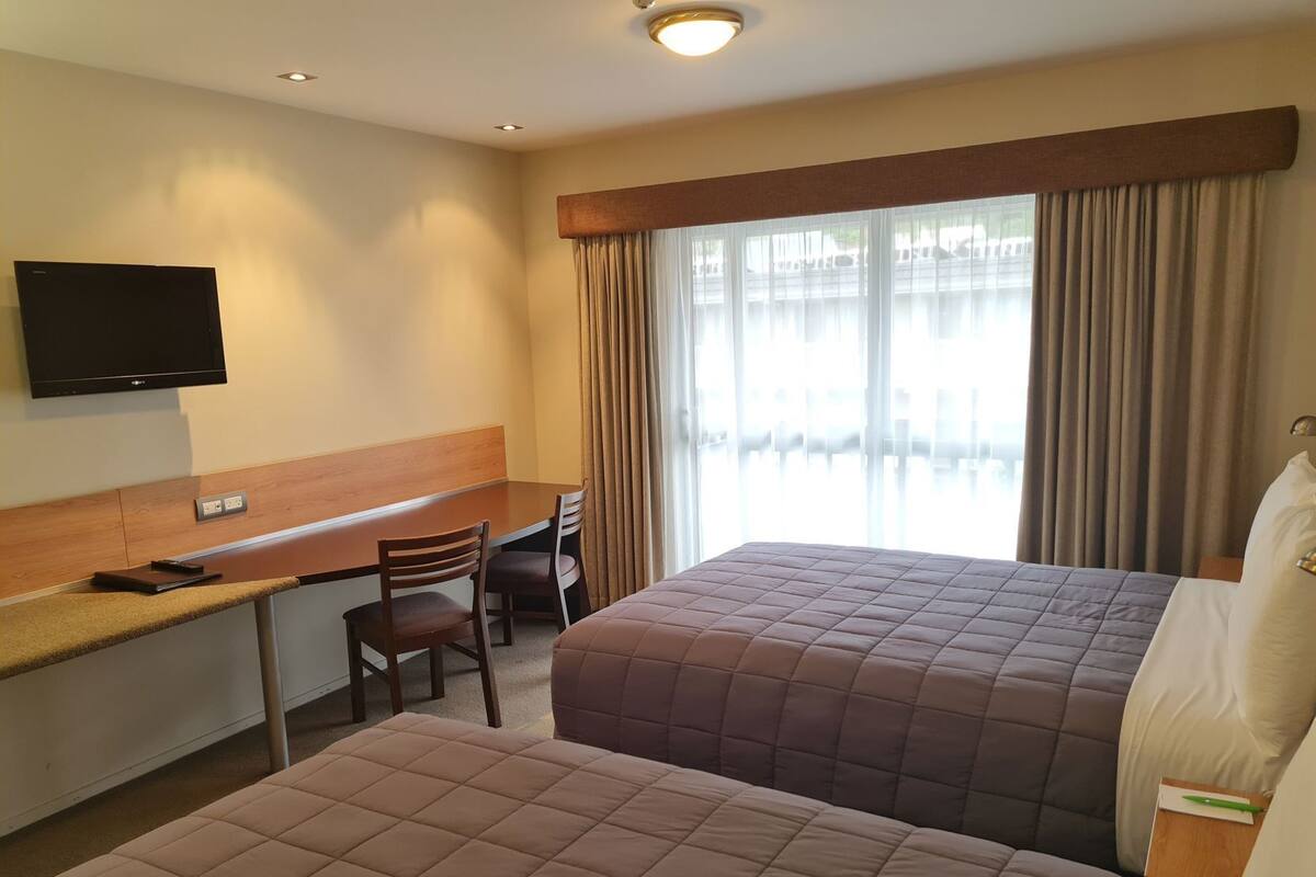 A hotel room with a bed, a desk, a chair, a television, and a window with curtains.