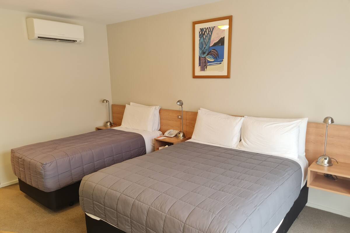 A hotel room with two beds, a nightstand with a phone, a lamp, and a framed artwork on the wall.