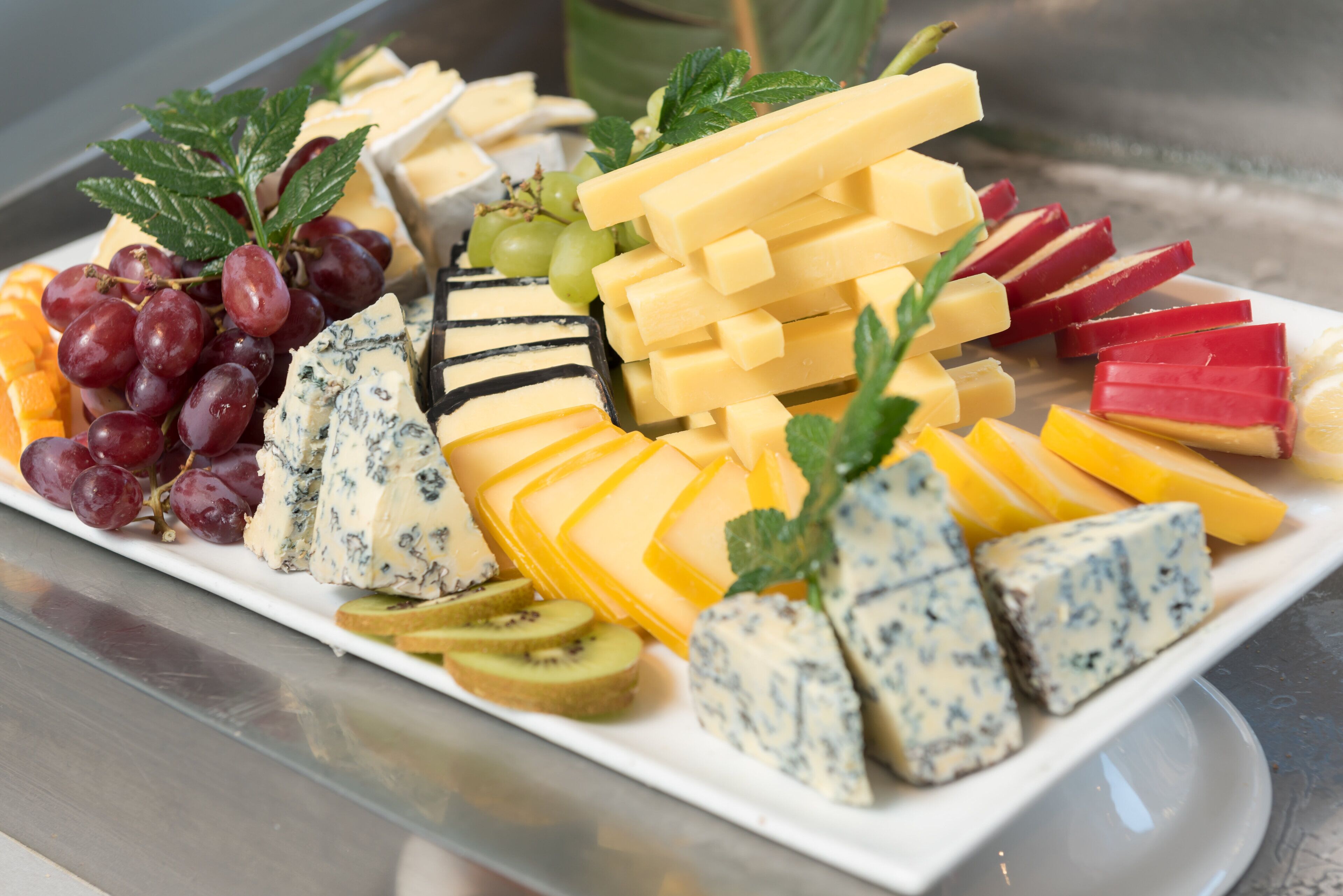 A variety of cheeses, fruits, and garnishes on a white platter.