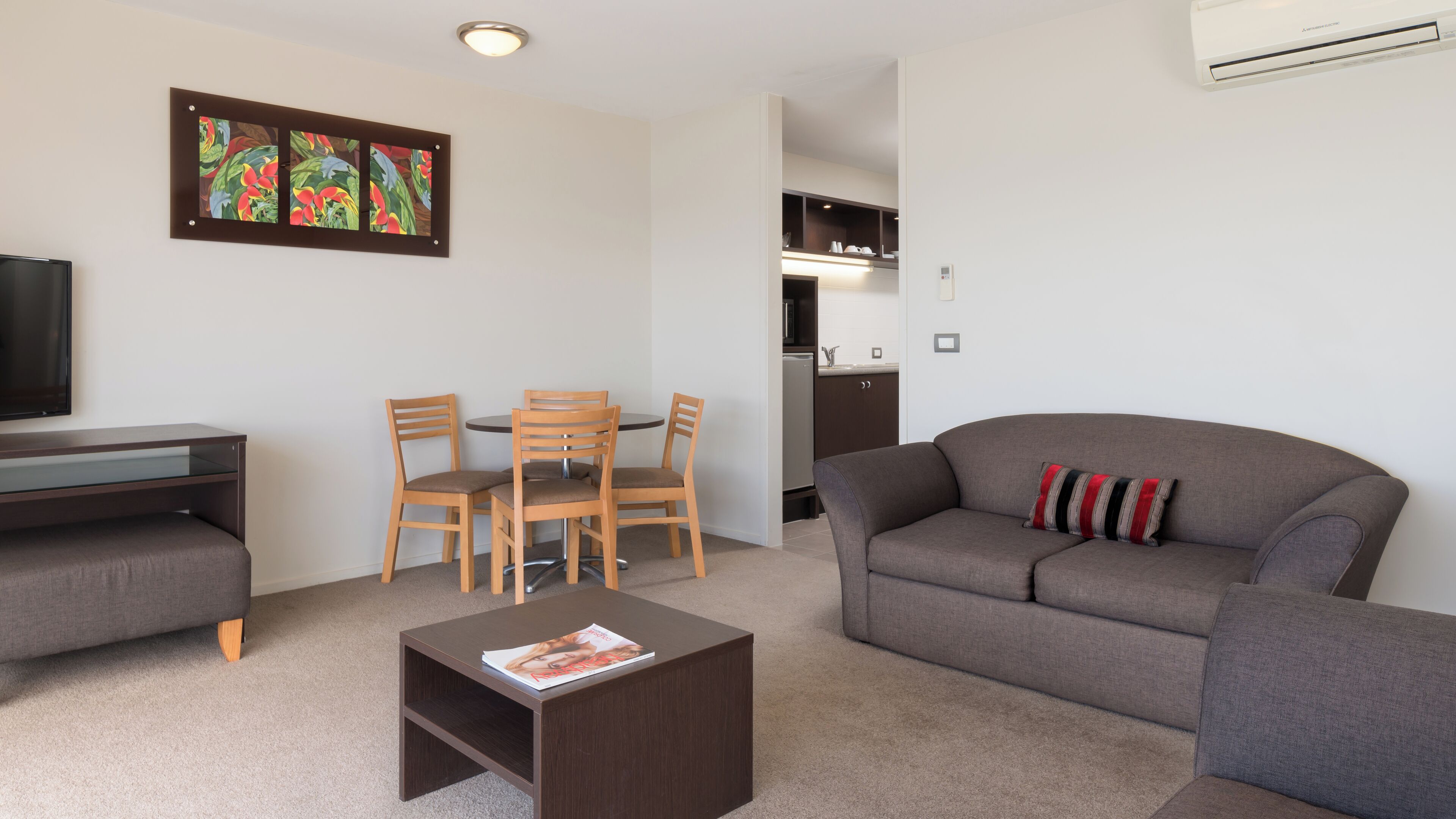 A modern living room with a grey sofa, wooden chairs, a coffee table, and a flat-screen TV.