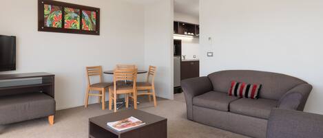 A modern living room with a grey sofa, wooden chairs, a coffee table, and a flat-screen TV.