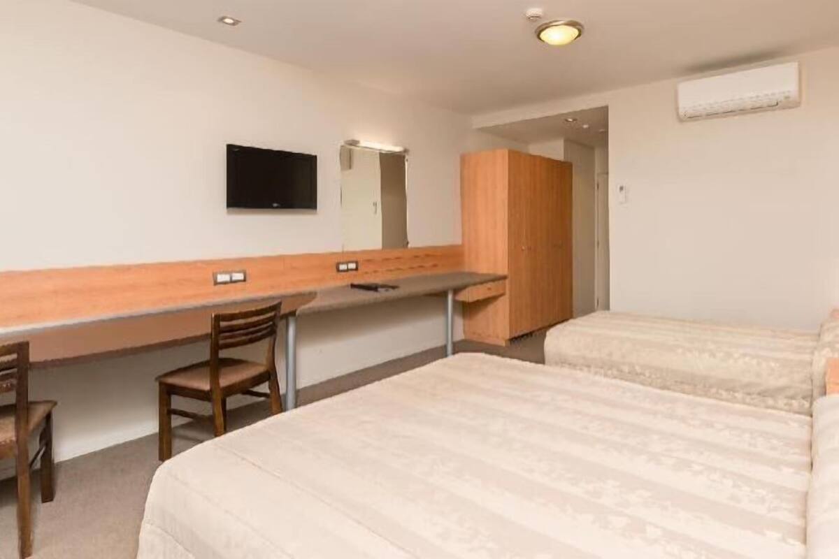 A hotel room with two beds, a desk, a chair, a TV, and a wardrobe.