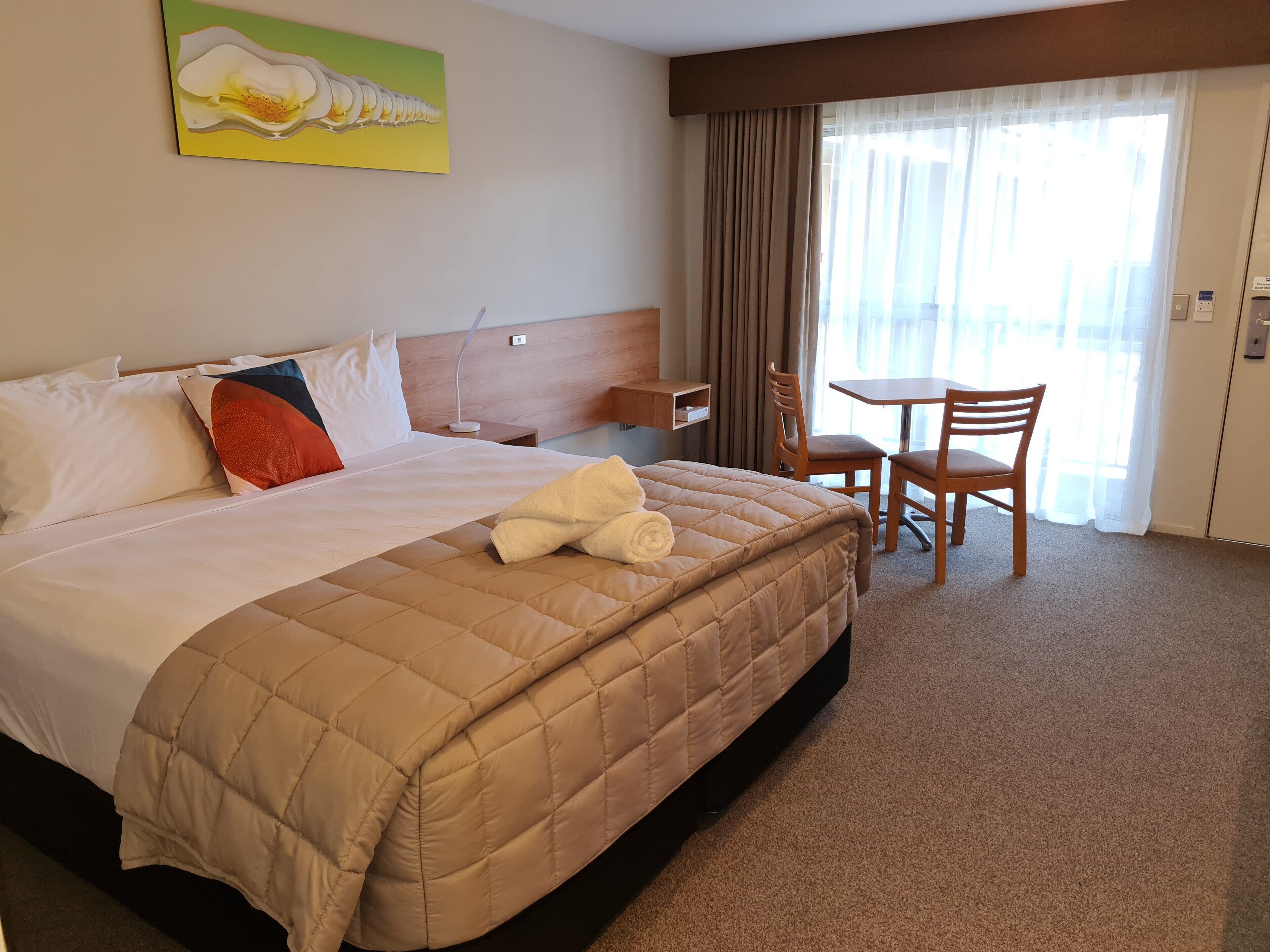 A hotel room with a large bed, a desk, a chair, and a window with curtains.