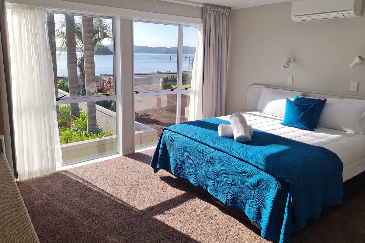 A hotel room with a bed, a view of the sea, and a sliding glass door.