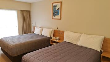 A hotel room with two beds, a nightstand with a lamp, a painting on the wall, and a window with curtains.