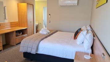 A hotel room with a bed, bedside table, and a desk with a chair.