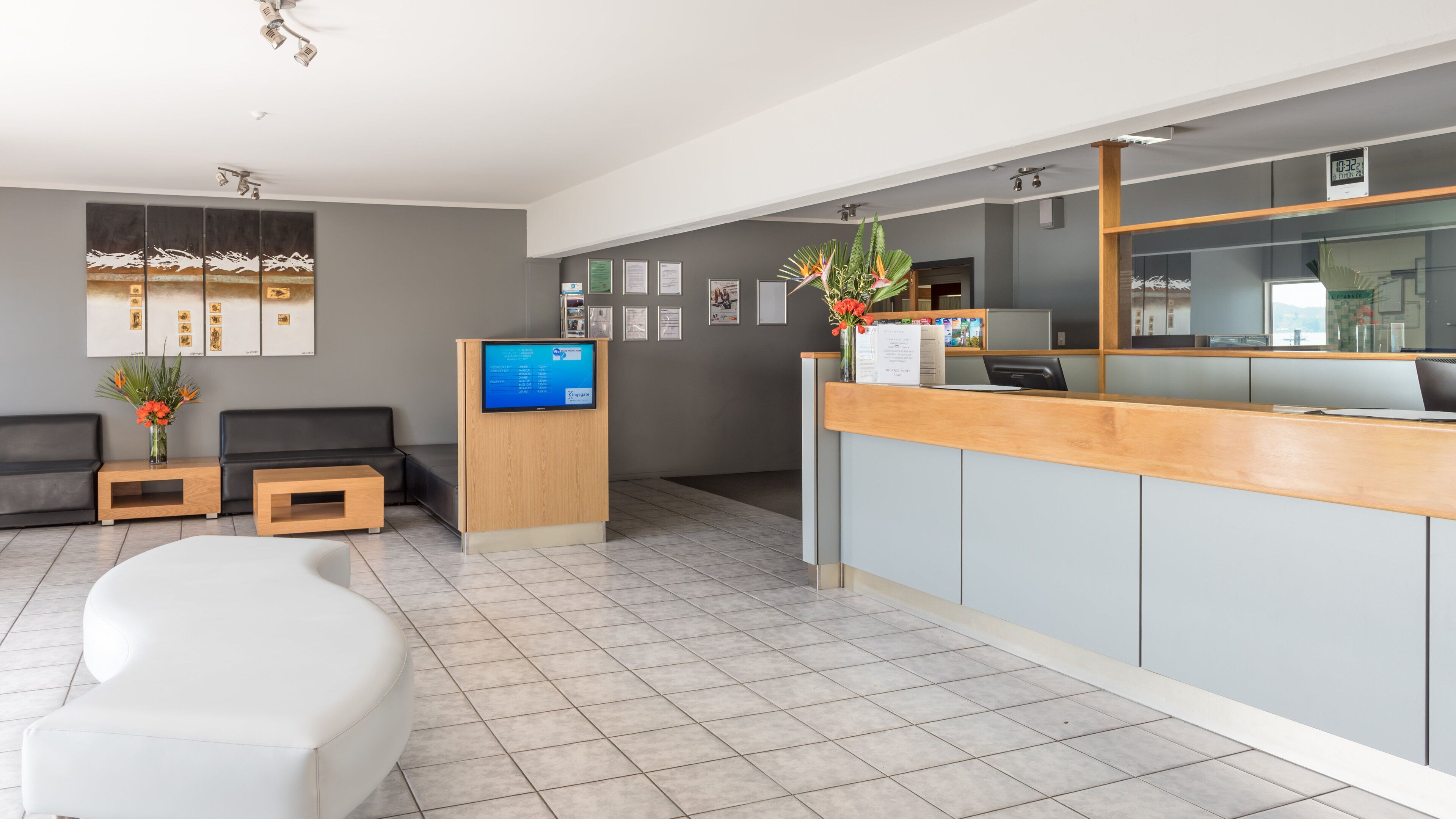Un espace d’accueil moderne avec un bureau en bois, un écran numérique, un coin salon avec un canapé et un pouf, et des certificats encadrés accrochés au mur.