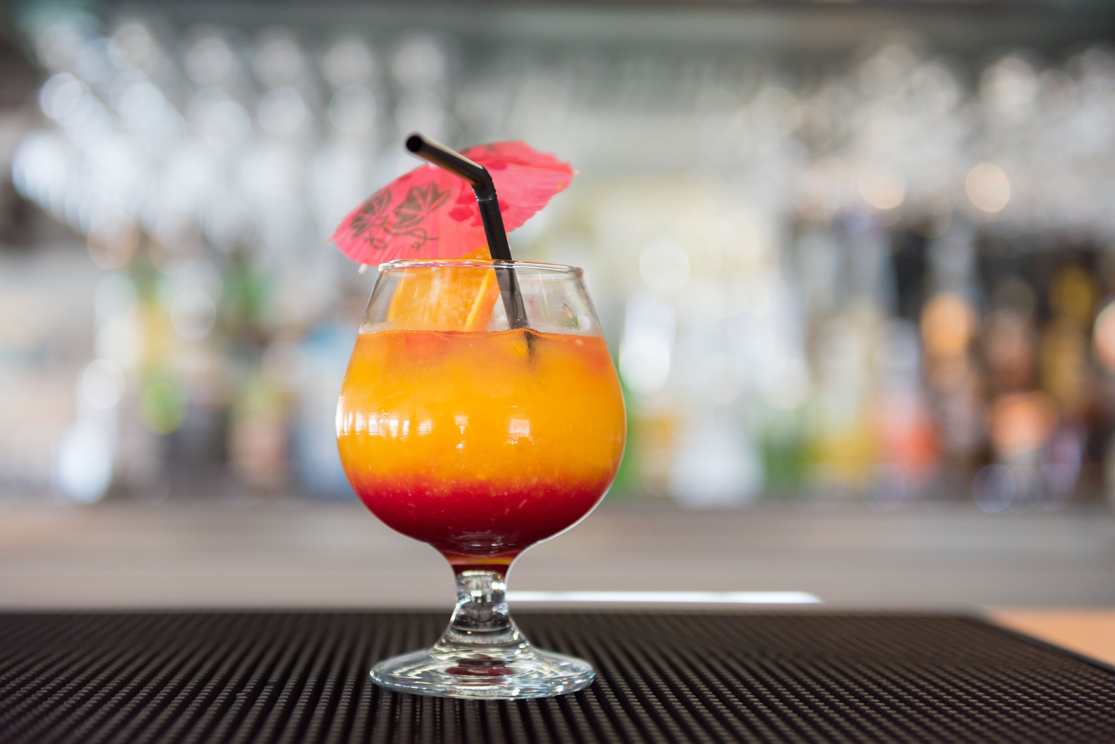 A cocktail in a glass with a straw and a decorative umbrella on a table.