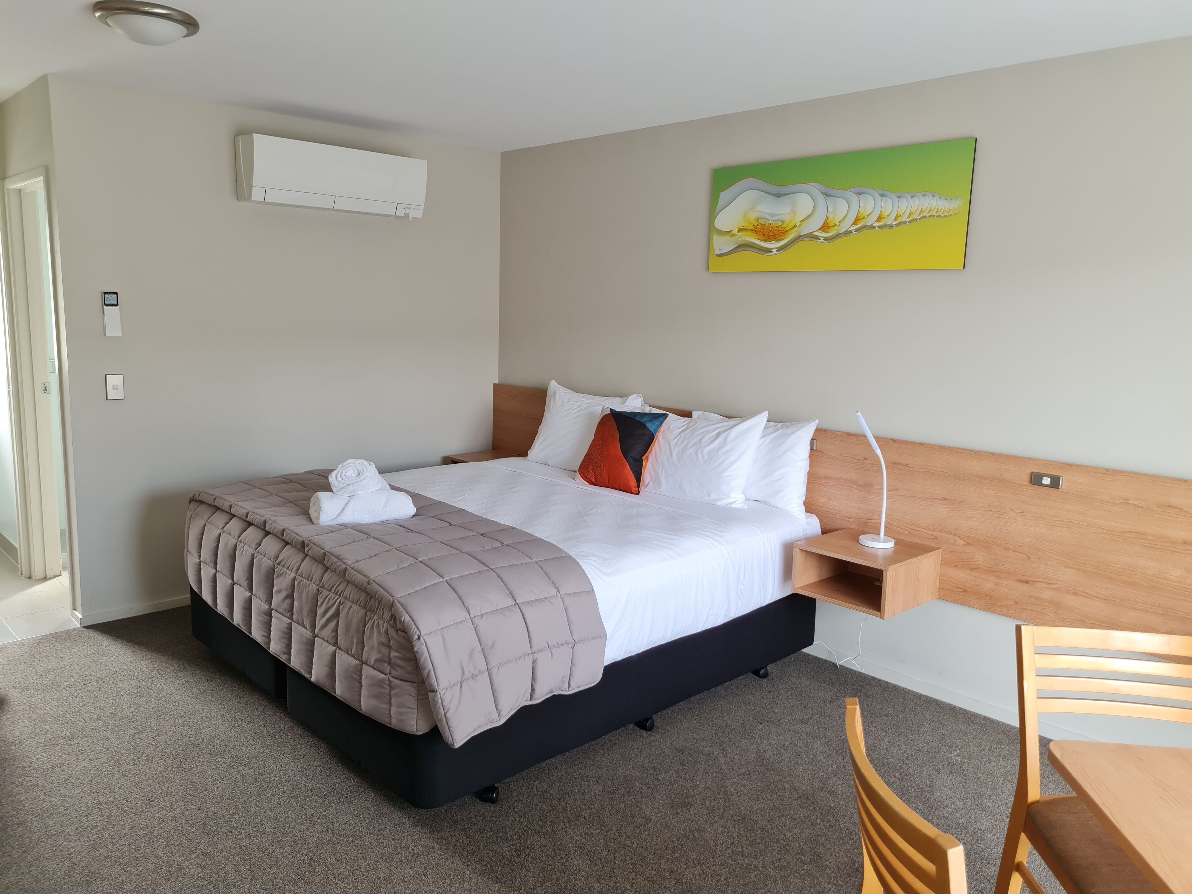 Quarto de hotel com cama, mesa de cabeceira, cadeira e um quadro na parede.