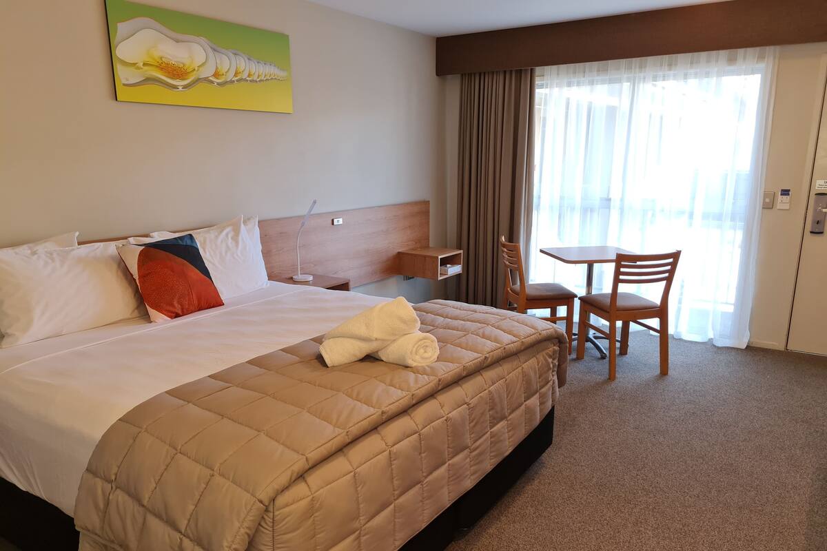 A hotel room with a bed, a desk, a chair, and a window with curtains.