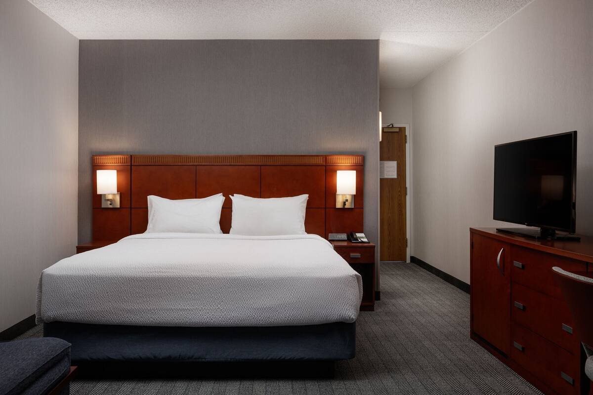 A hotel room with a large bed, two bedside lamps, a TV on a wooden cabinet, and a door in the background.