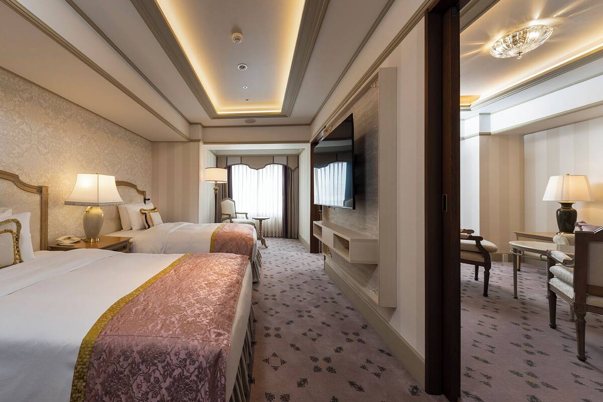 A hotel room with two beds, a TV, a desk, and a chair.