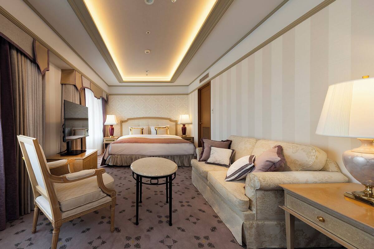 A hotel room with a bed, a sofa, a chair, a small table, and a TV.