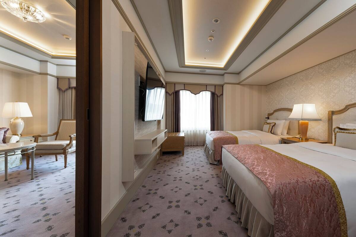 A hotel room with two beds, a desk, a chair, and a television.