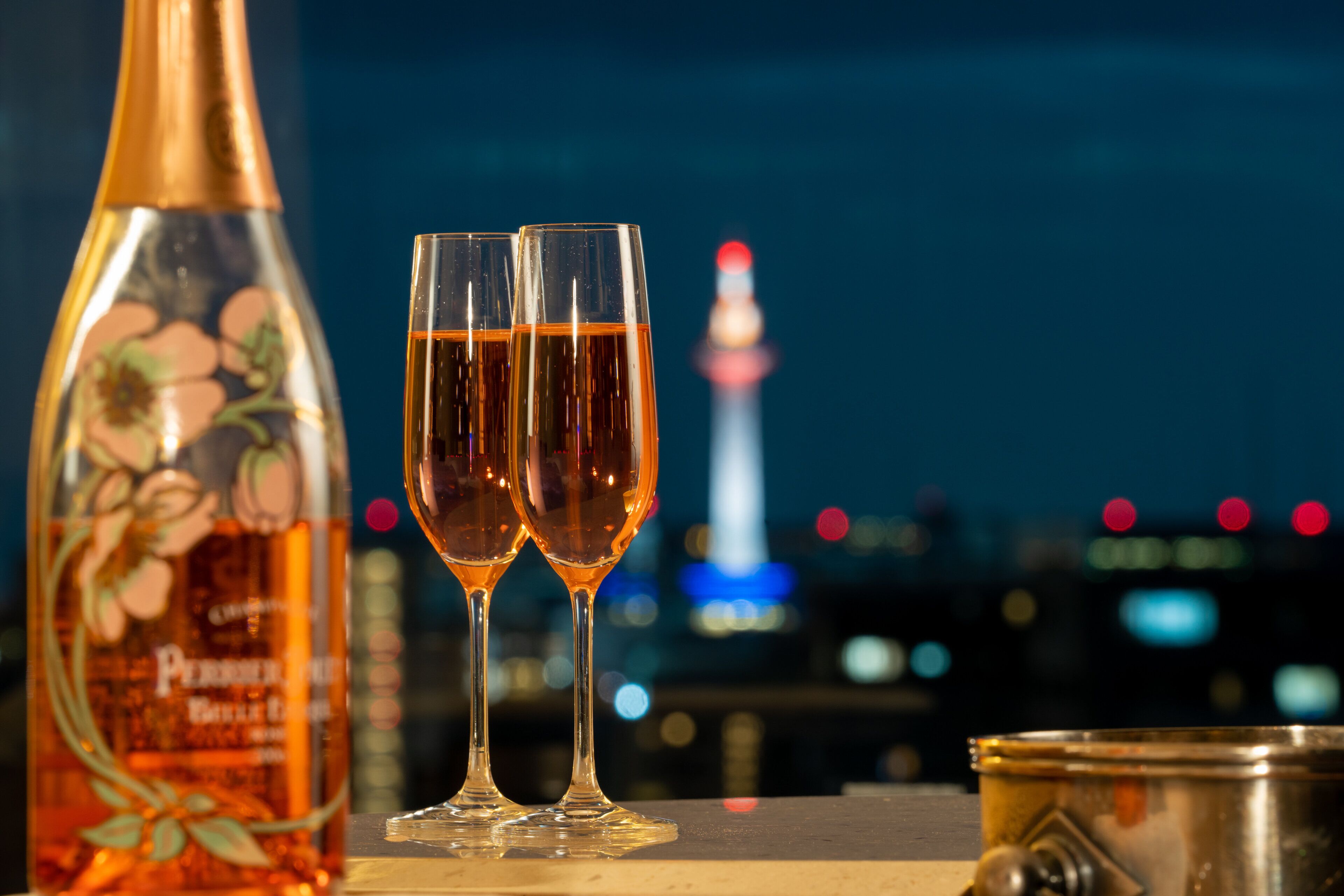A bottle of Perrier wine and two glasses on a table with a cityscape in the background.