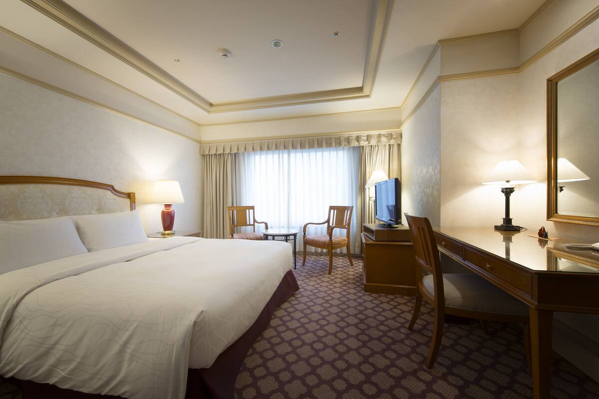 A hotel room with a large bed, a desk, a chair, a television, and a mirror.