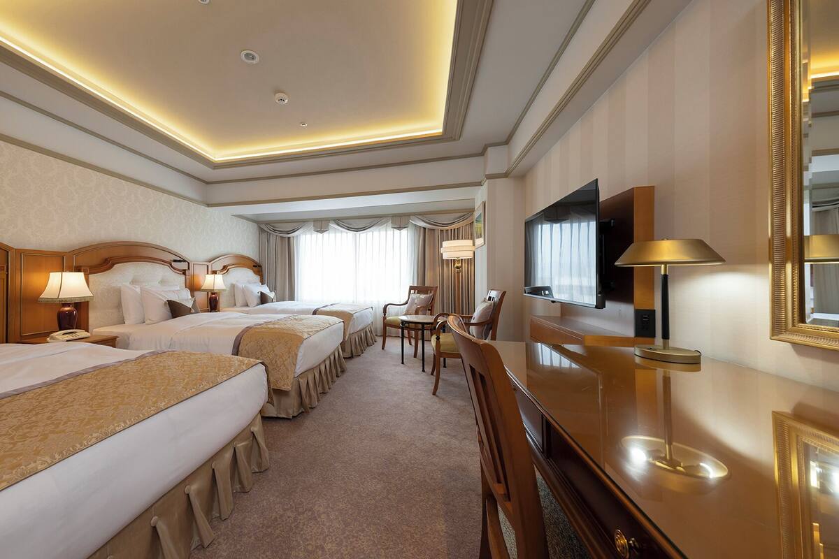 A hotel room with two beds, a desk, a chair, a TV, and a mirror.