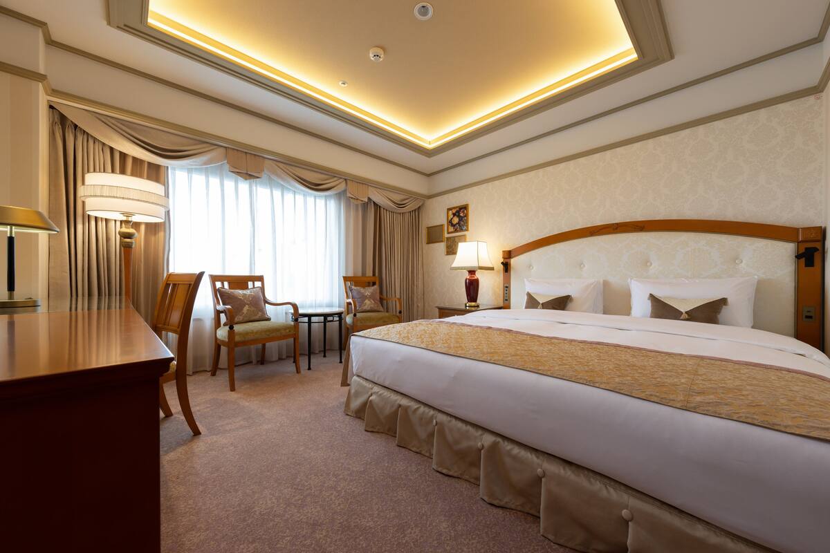 A hotel room with a large bed, a desk, a chair, and a lamp.