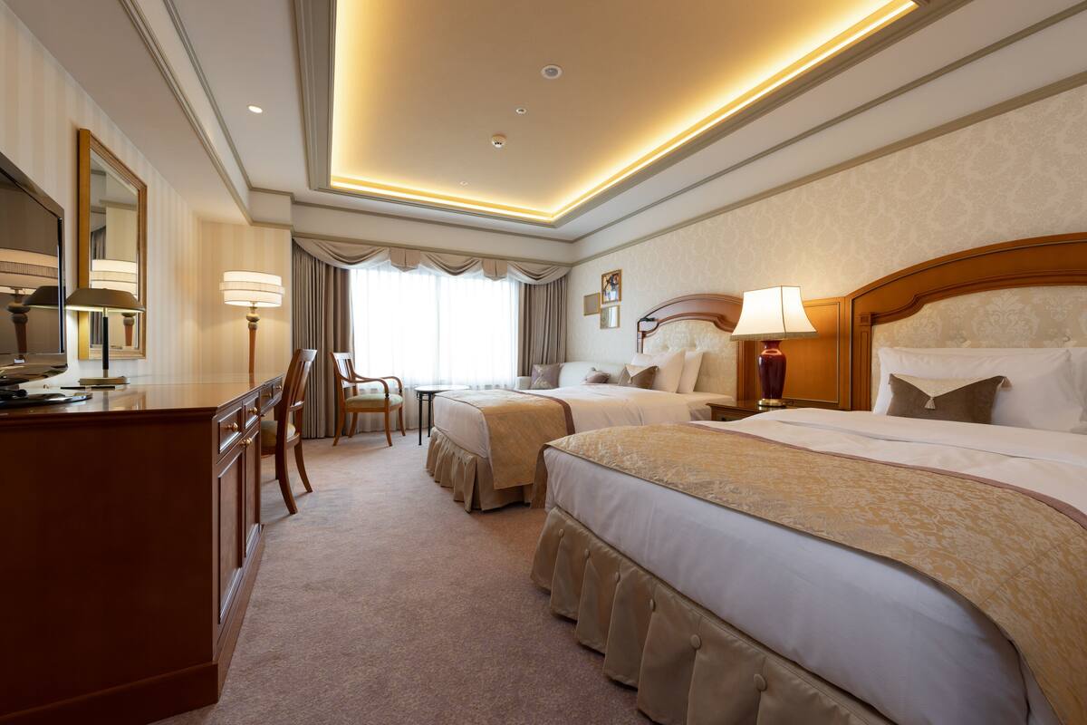 A hotel room with a large bed, a smaller bed, a desk, and a chair.