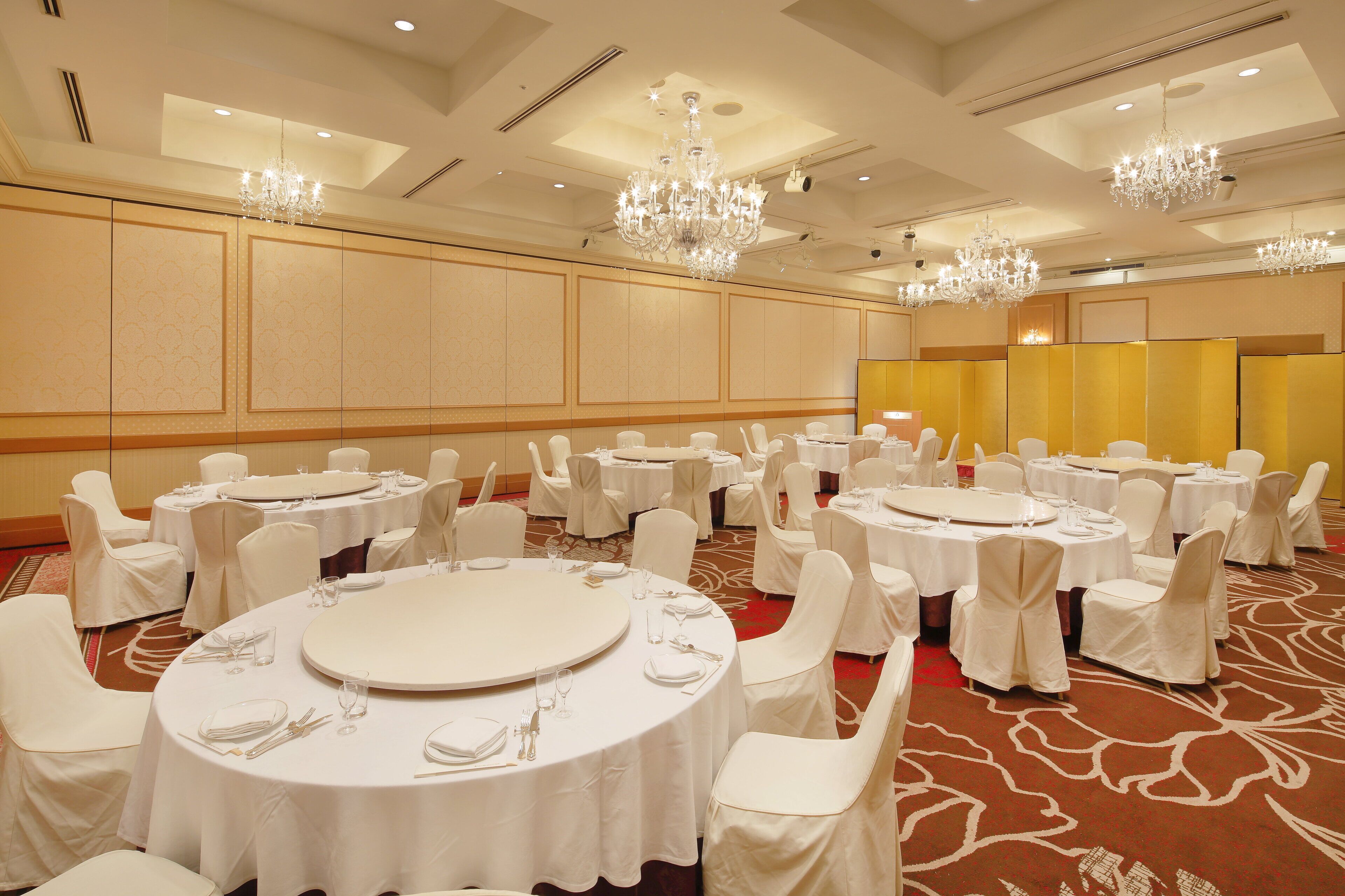 Un salón de banquetes con mesas redondas, sillas blancas y candelabros.