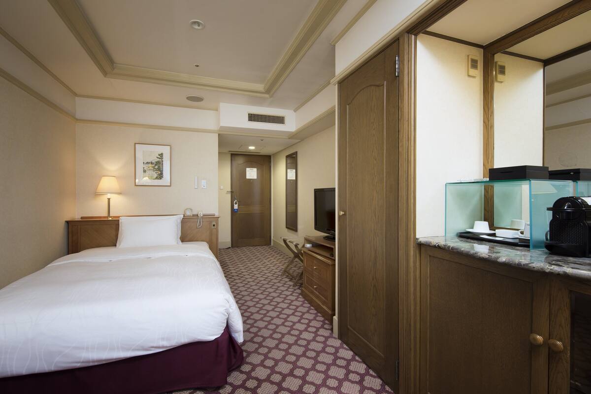A hotel room with a bed, a desk with a computer, a television, and a minibar.