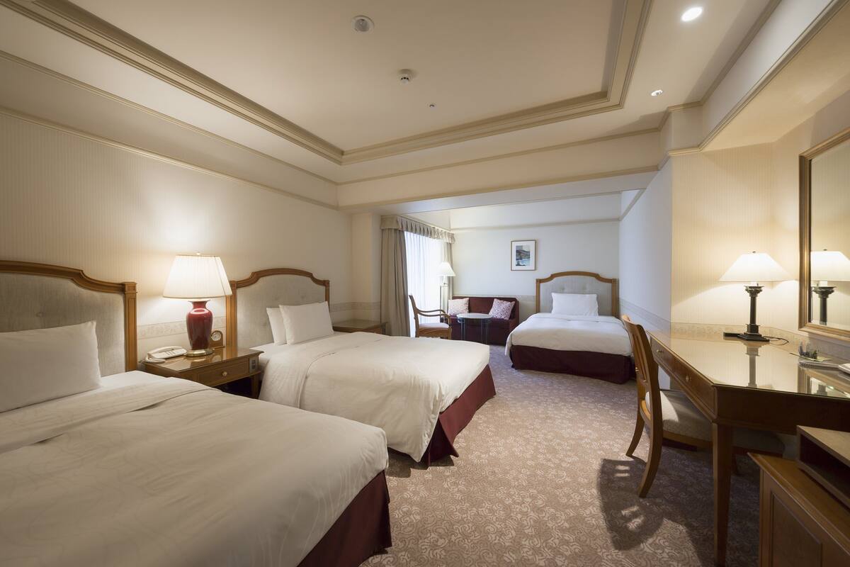 A hotel room with two beds, a desk, a chair, and a small table.