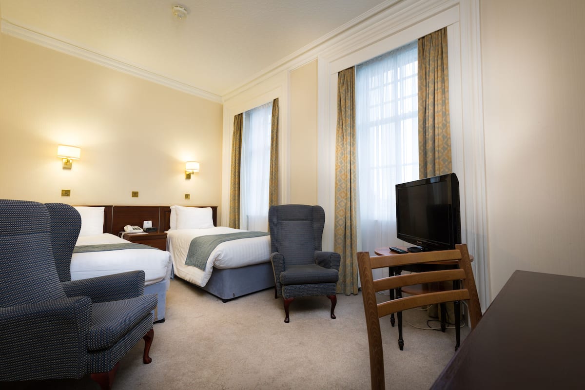 Une chambre d’hôtel avec deux lits, une télévision, un bureau et une chaise.