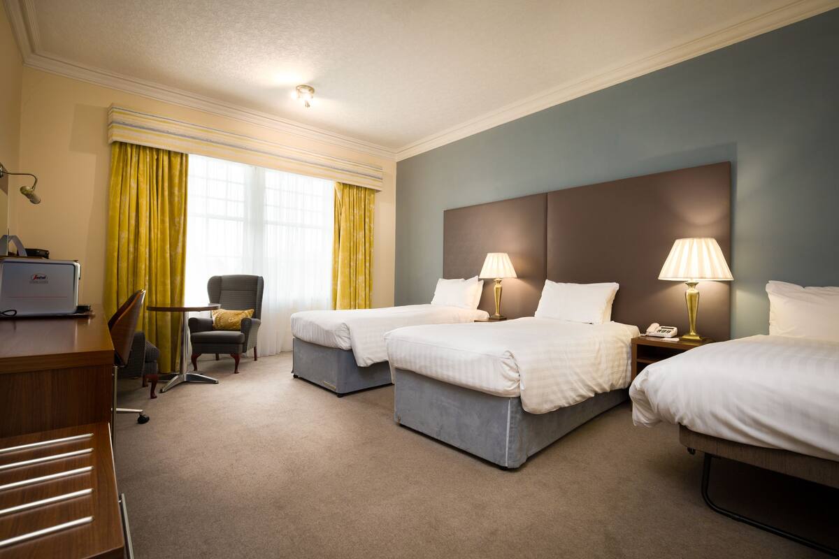 Une chambre d’hôtel avec deux lits simples, un bureau, une chaise et une lampe.