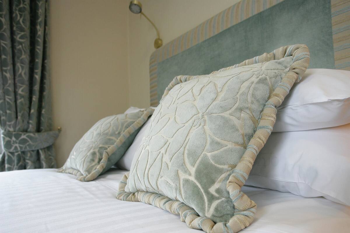 Un lit bien fait, agrémenté de deux coussins décoratifs et d’un coussin uni blanc.